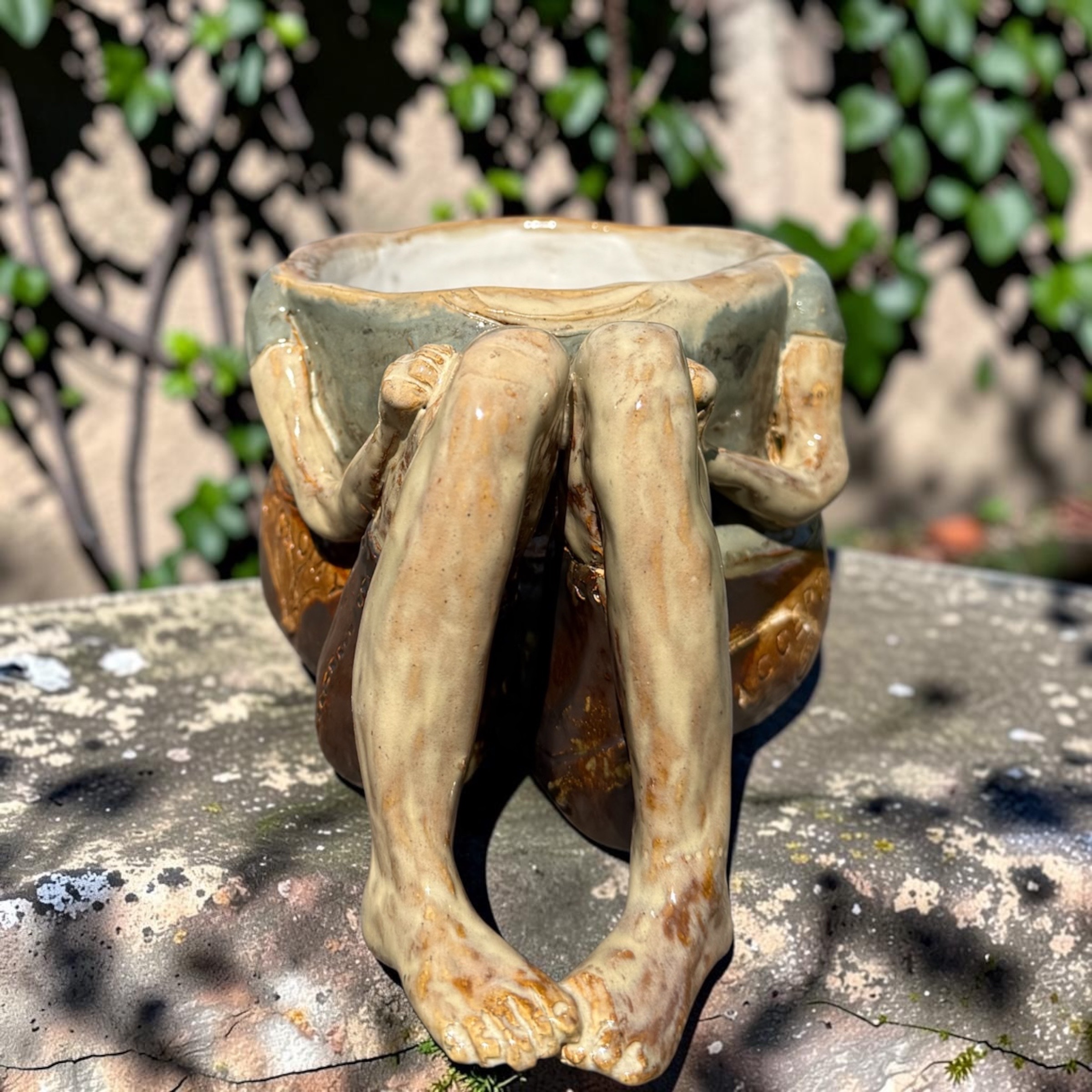 a ceramic vessel formed from a crouching figure's legs and feet, cupping the bowl above